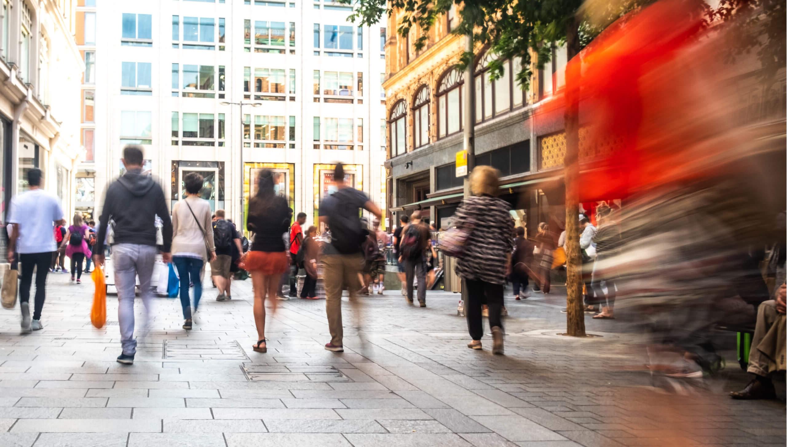 Various people walking in a street with shops either side, some carrying shopping bags. 蓝色对一些人的影响.